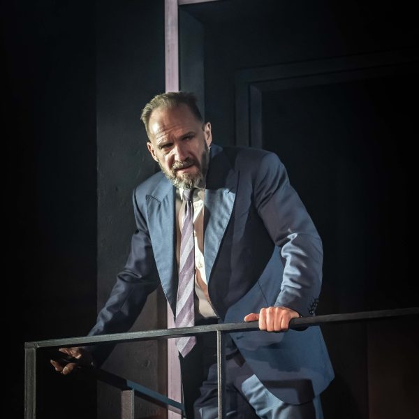 Ralph Fiennes as Macbeth. He looks haggard and wears a navy blue suit